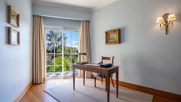 Quarto com escrivaninha de madeira, uma cadeira, janela com cortinas e luminária fixada na parede.