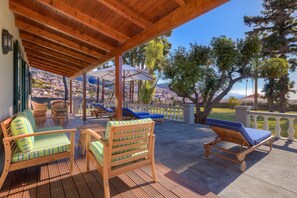Un espacio de estar al aire libre cubierto, con mobiliario de madera y vistas a un pueblo en la ladera.