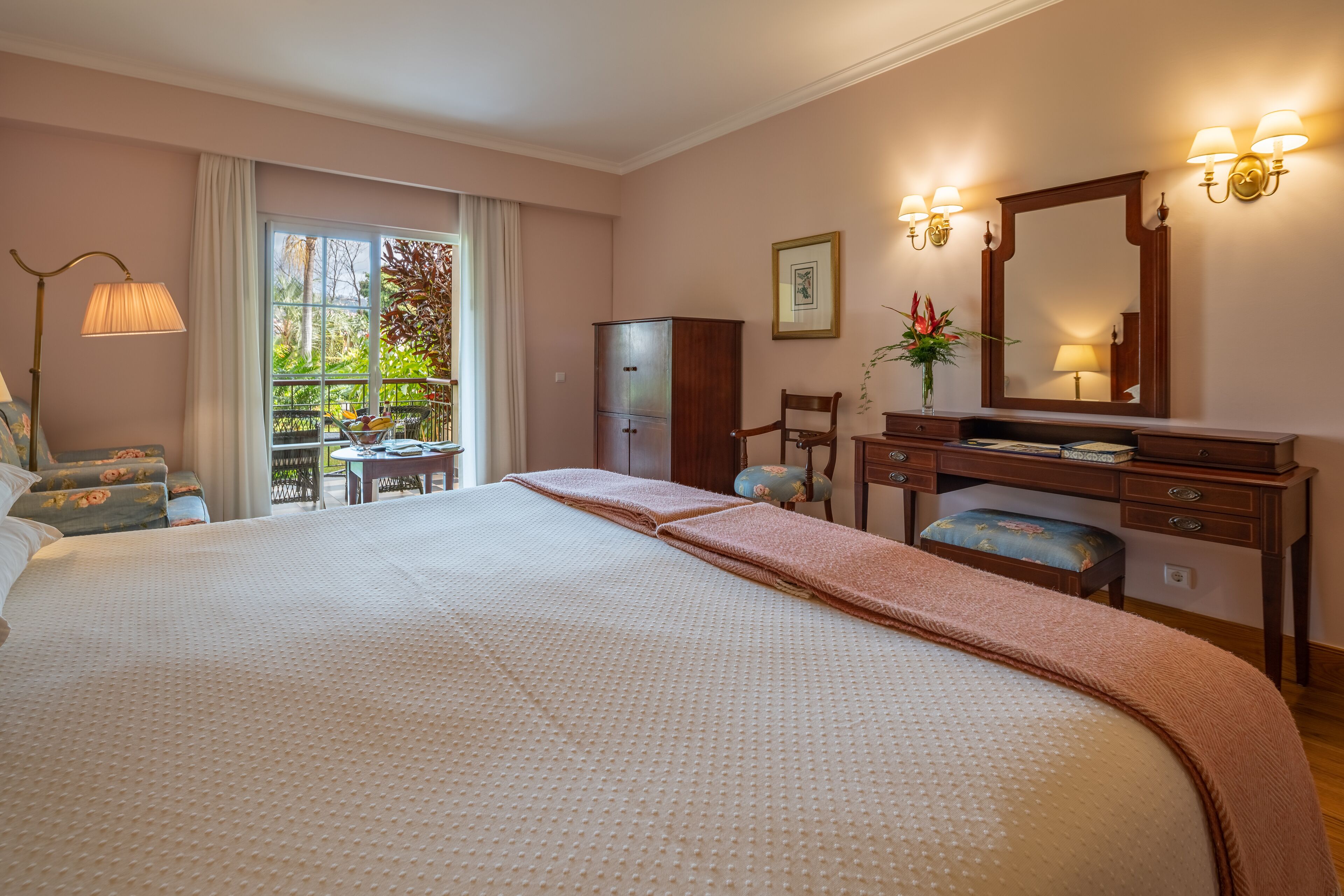 Habitación de hotel con una cama grande, un escritorio con silla, un armario y un ventanal con vistas al verde.