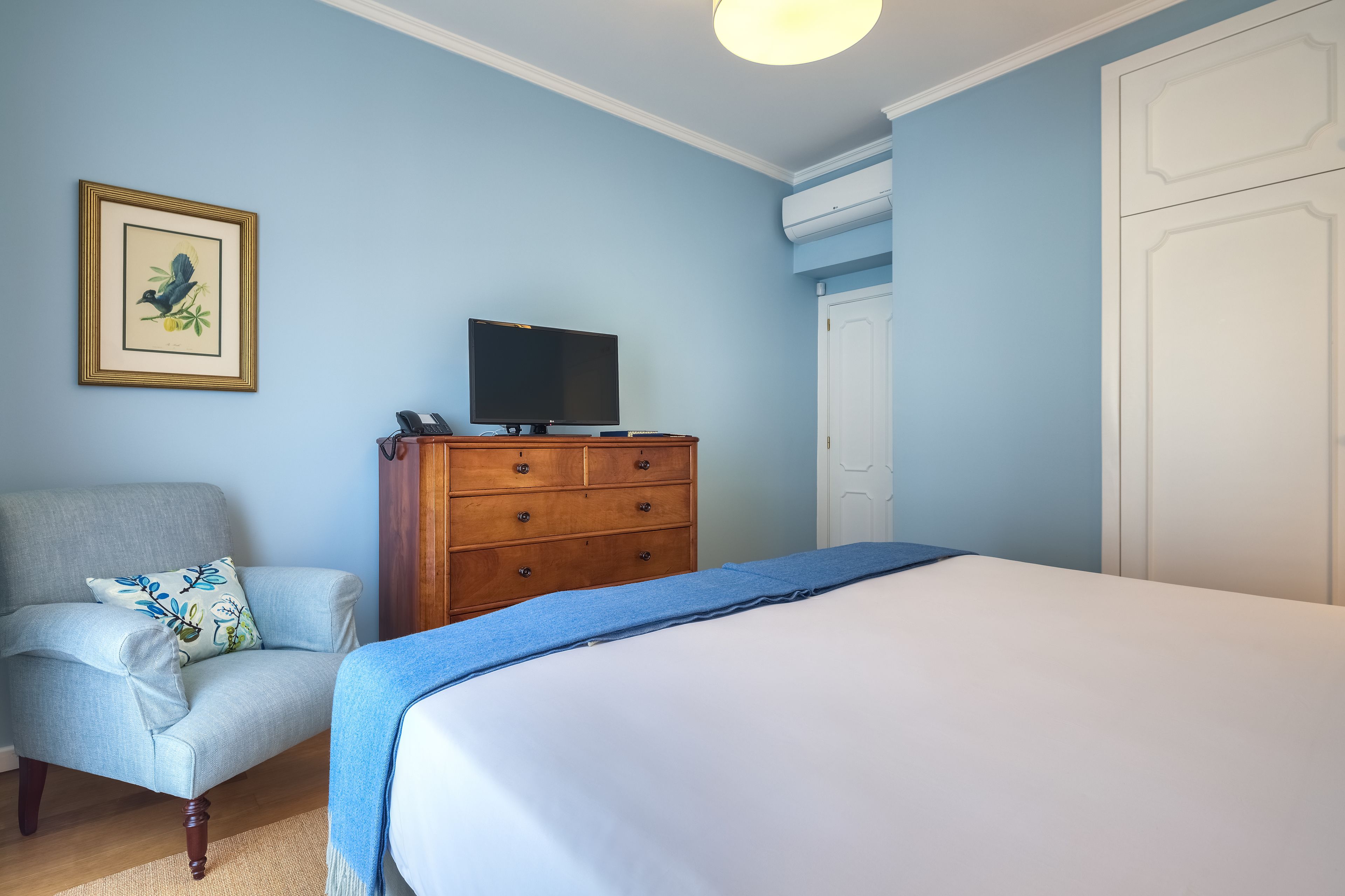 A bedroom with a bed, a dresser, a chair, a television, and a framed picture on the wall.