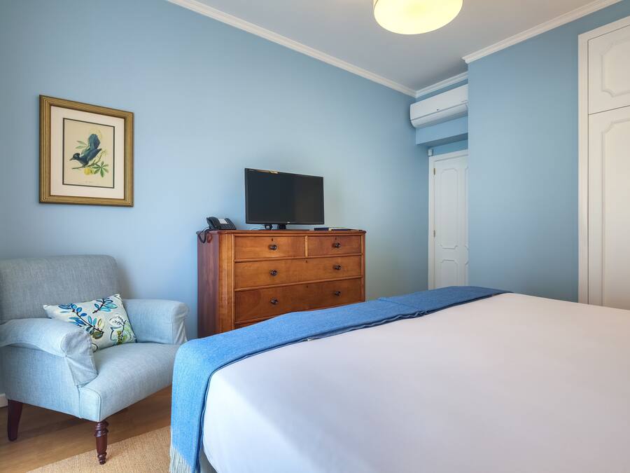 A bedroom with a bed, a dresser, a chair, a television, and a framed picture on the wall.