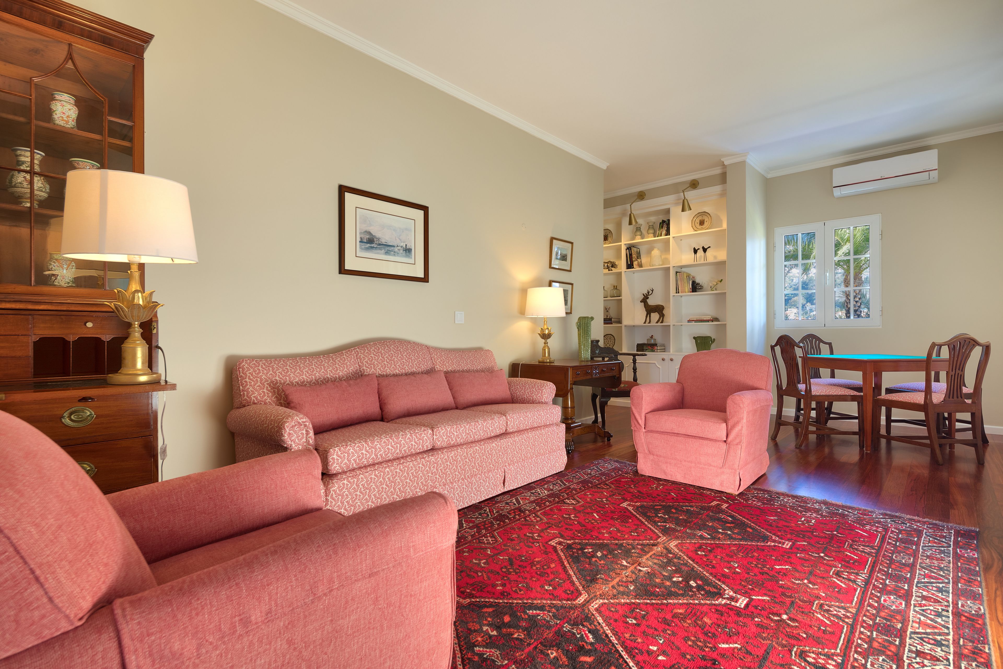 Un salon avec un tapis à motifs rouges, un canapé, un fauteuil, une lampe et un coin repas comprenant des chaises et une table.