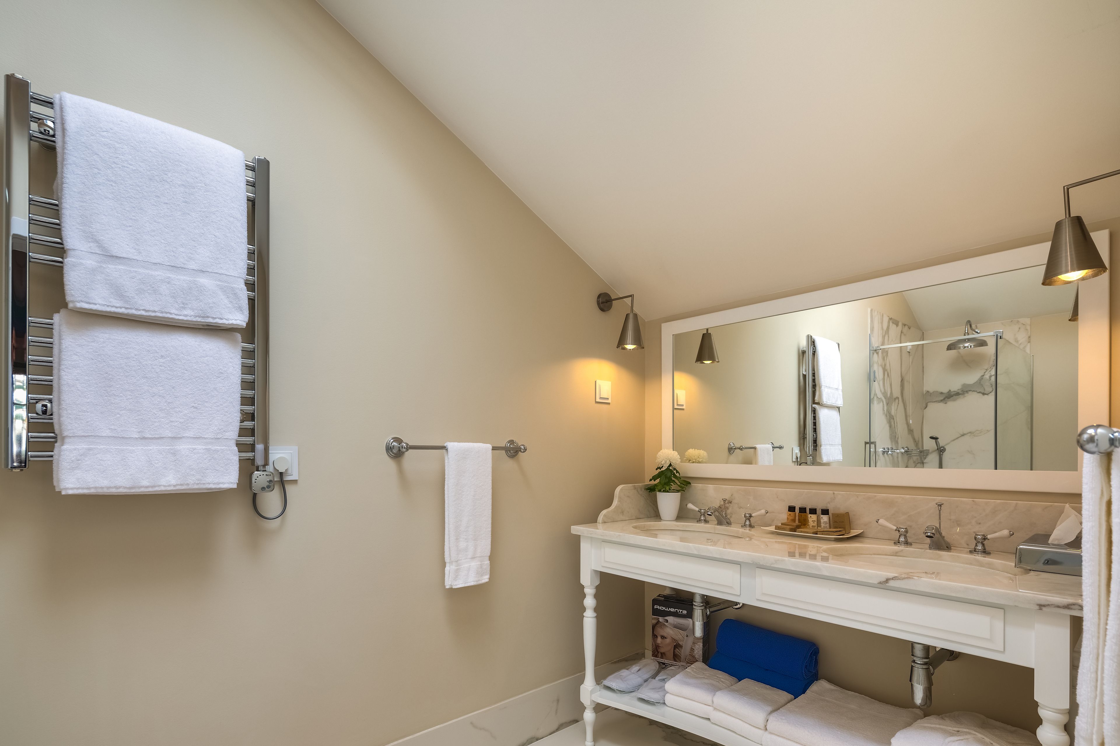 Een badkamer met een witte wastafel, een grote spiegel en een handdoekrek met twee handdoeken.