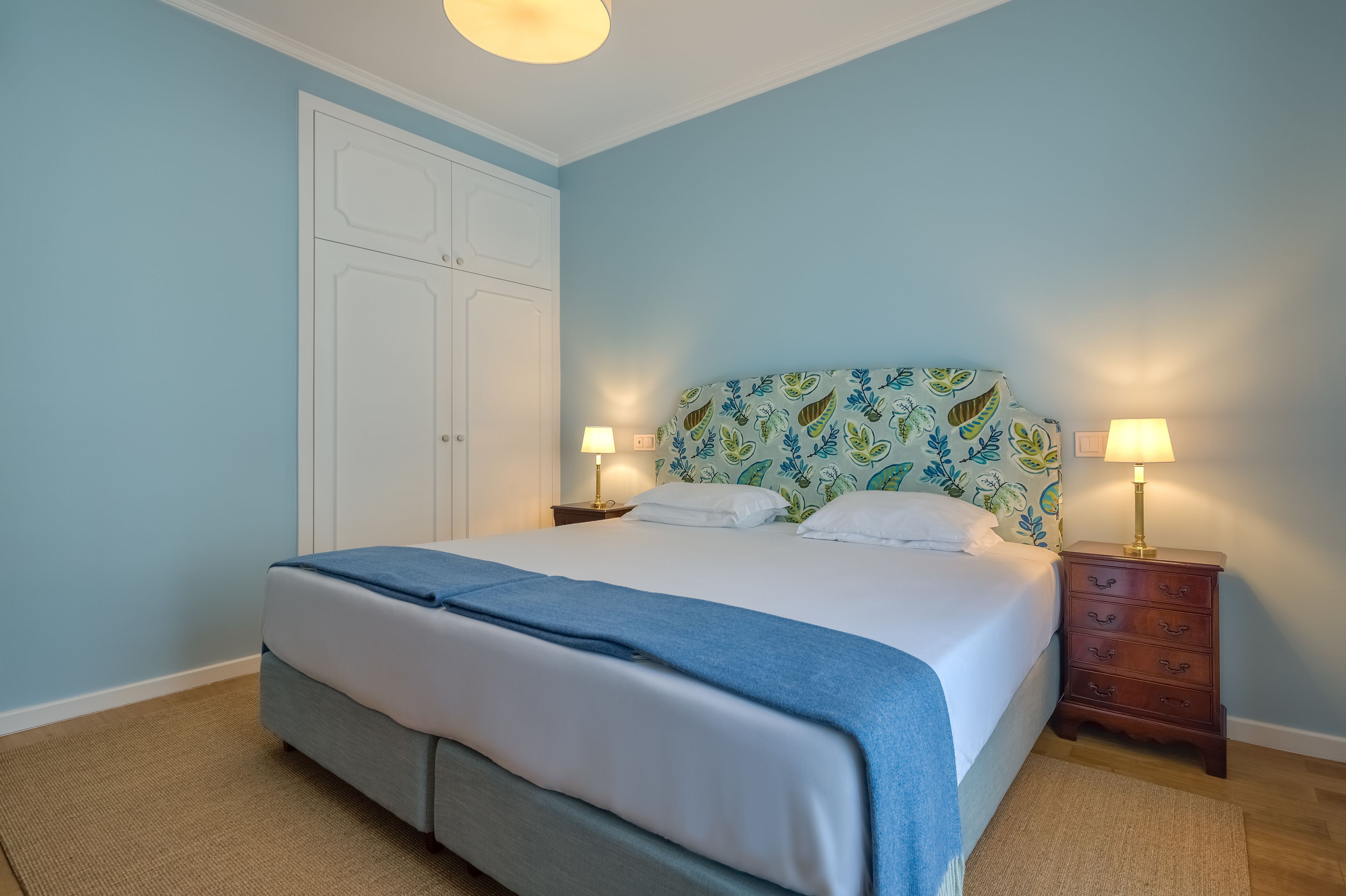 A bedroom with a bed, two bedside tables with lamps, a wardrobe, and a patterned headboard.