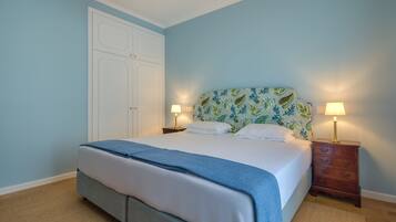 A bedroom with a bed, two bedside tables with lamps, a wardrobe, and a patterned headboard.