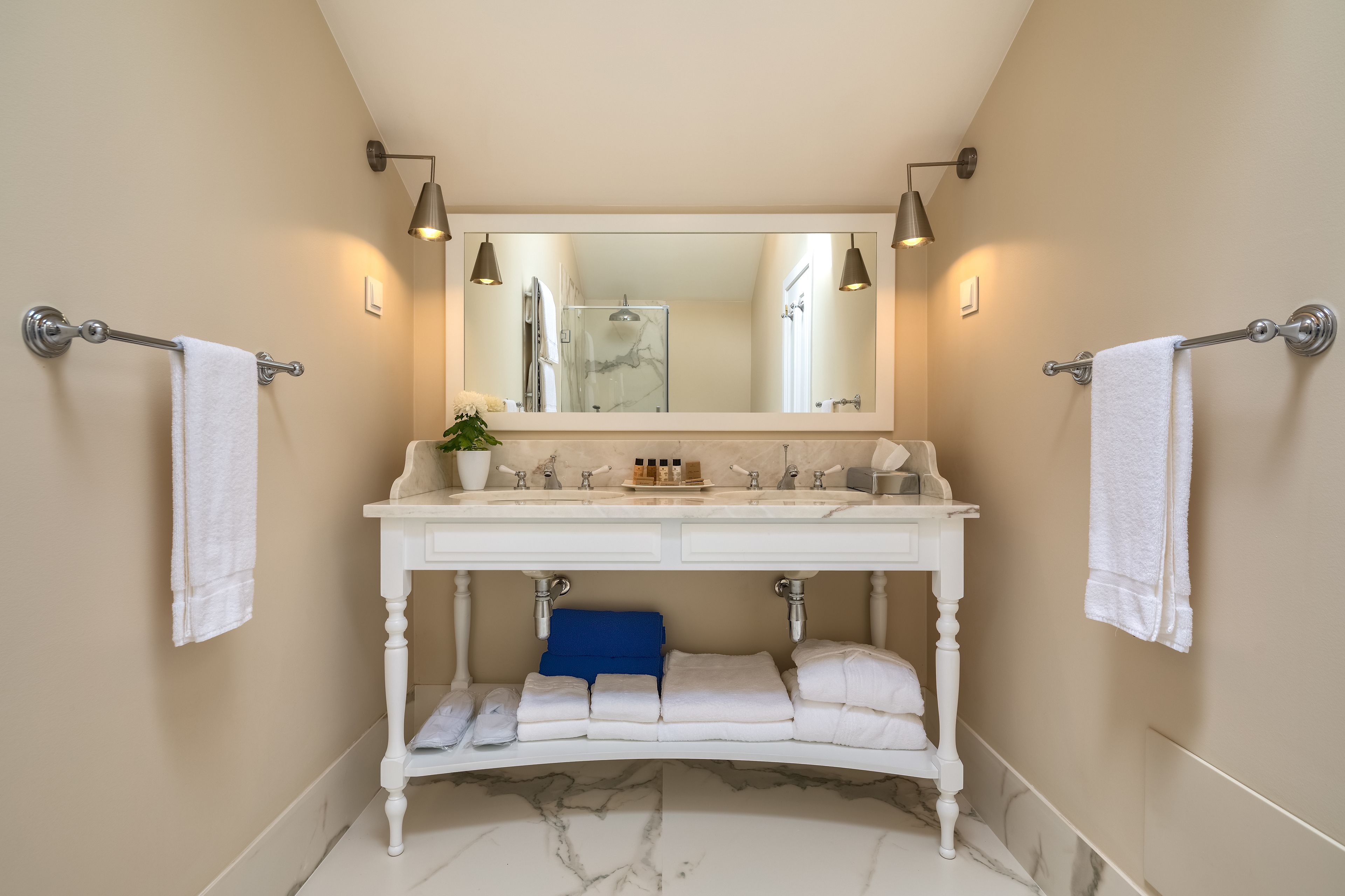 A bathroom with a white vanity, two towel racks, a mirror, and a blue towel on the shelf.