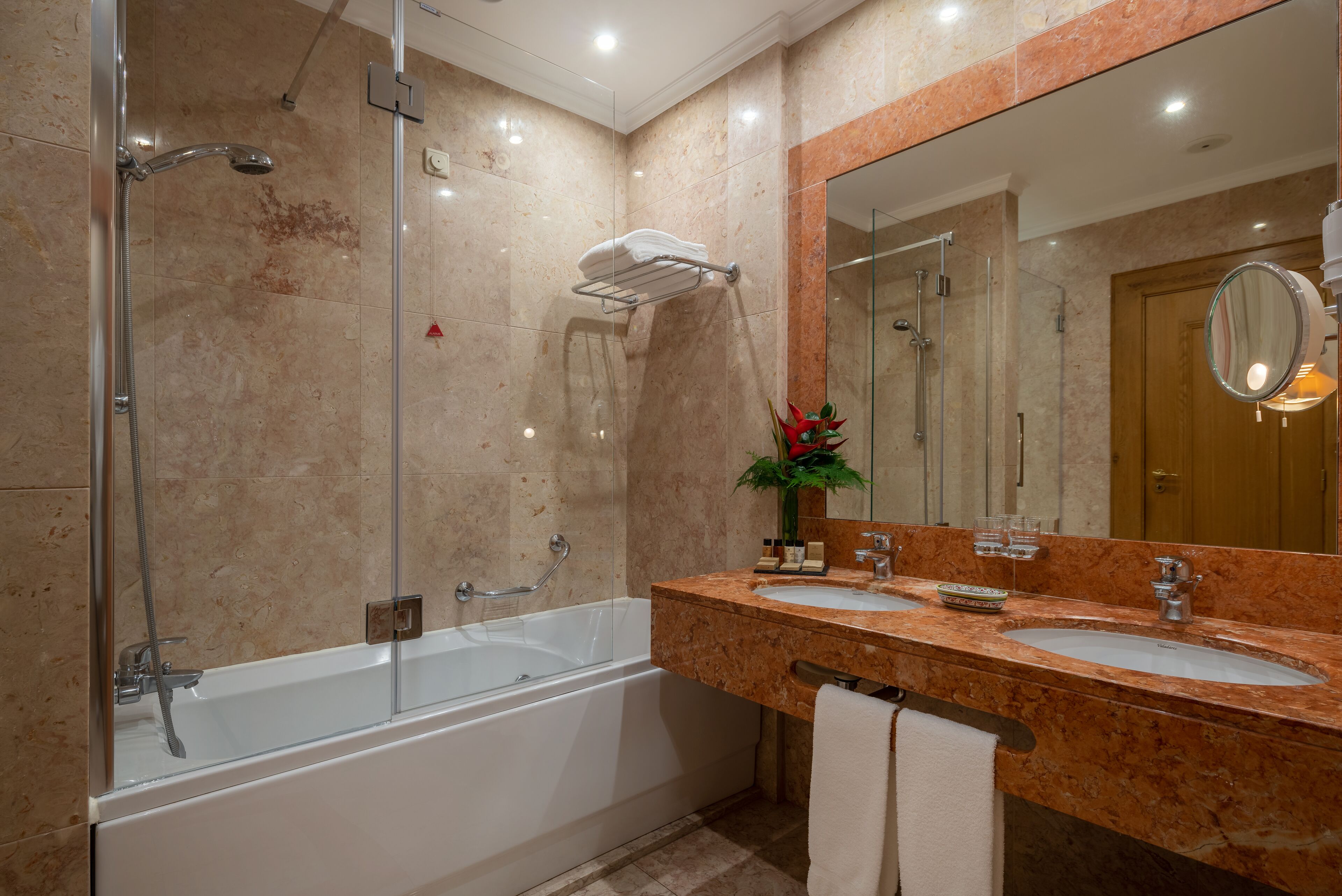 Un baño moderno con ducha envuelta en vidrio, bañera blanca y encimera de mármol con lavabo y tocador.