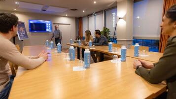 A conference room with a long table, chairs, a TV screen, and a window with curtains.