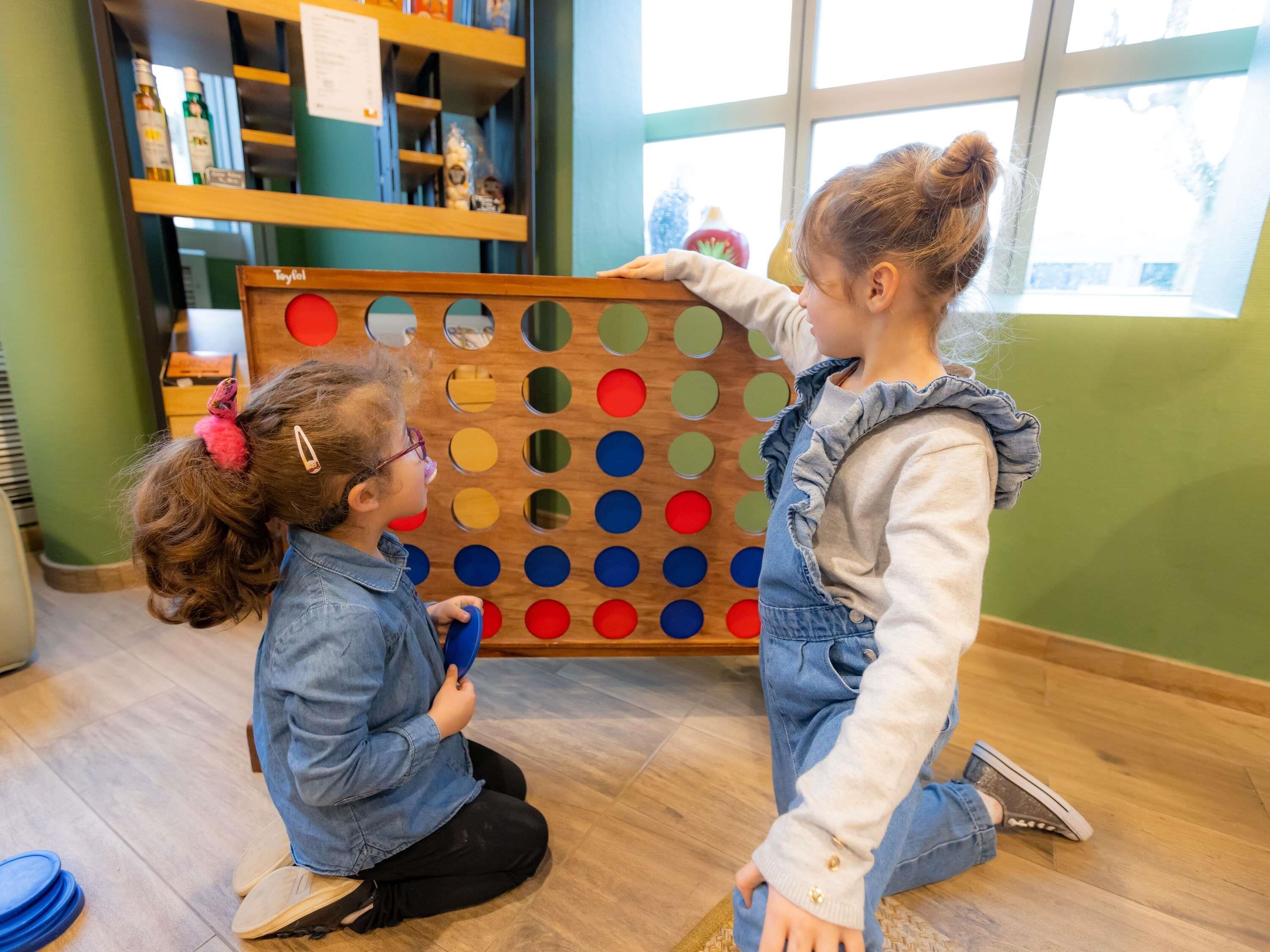 Dos niños jugando un juego de mesa en el interior, con una ventana al fondo.