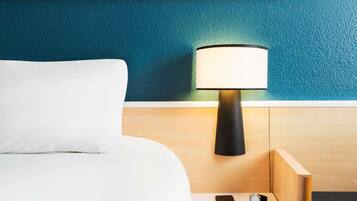 A hotel room with a bed, a nightstand, a lamp, a phone, and a watch.