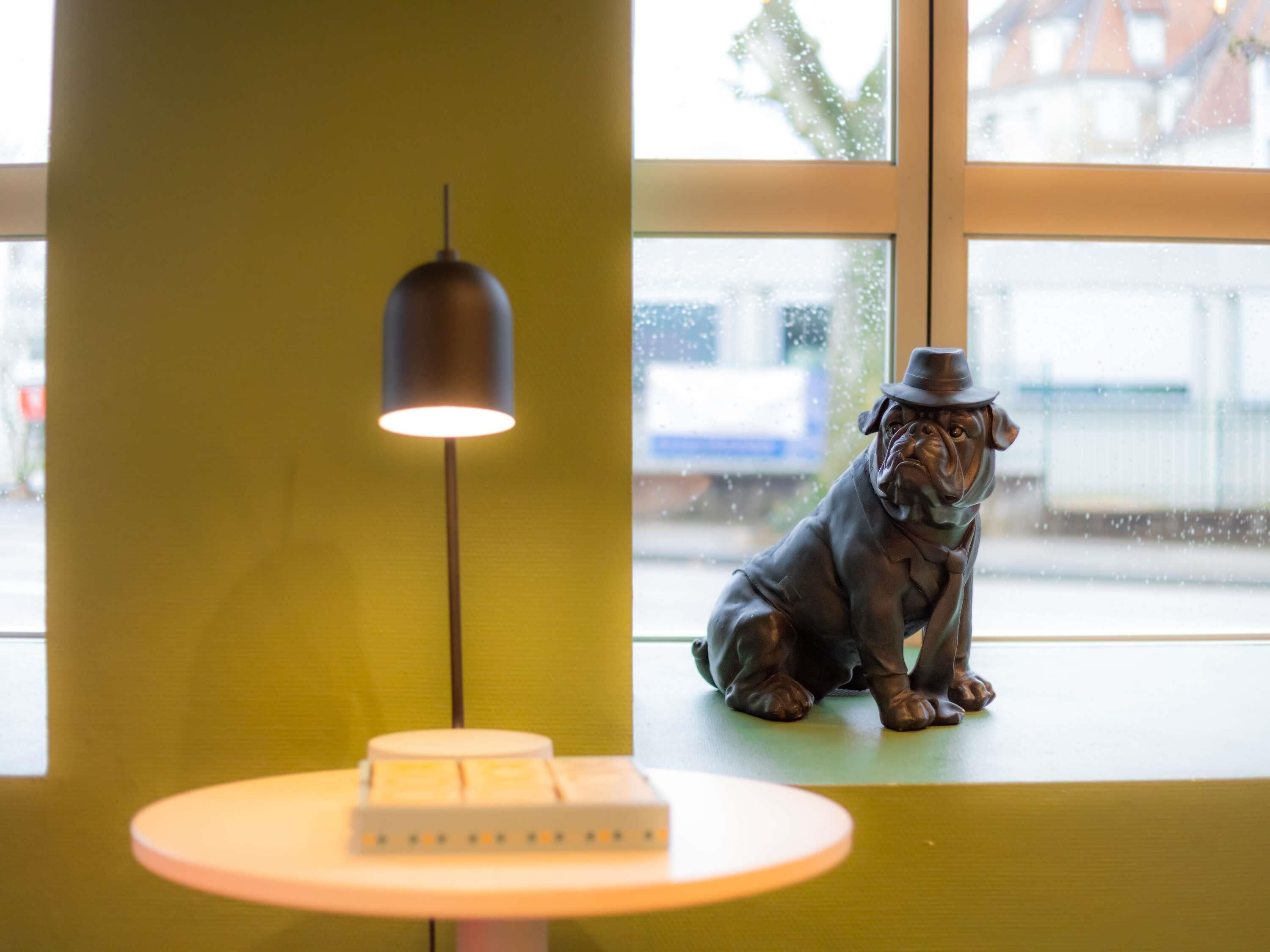Eine Statue eines Hundes, der auf einem Fensterbrett sitzt, eine Lampe und ein kleiner Tisch mit einer Kiste darauf.