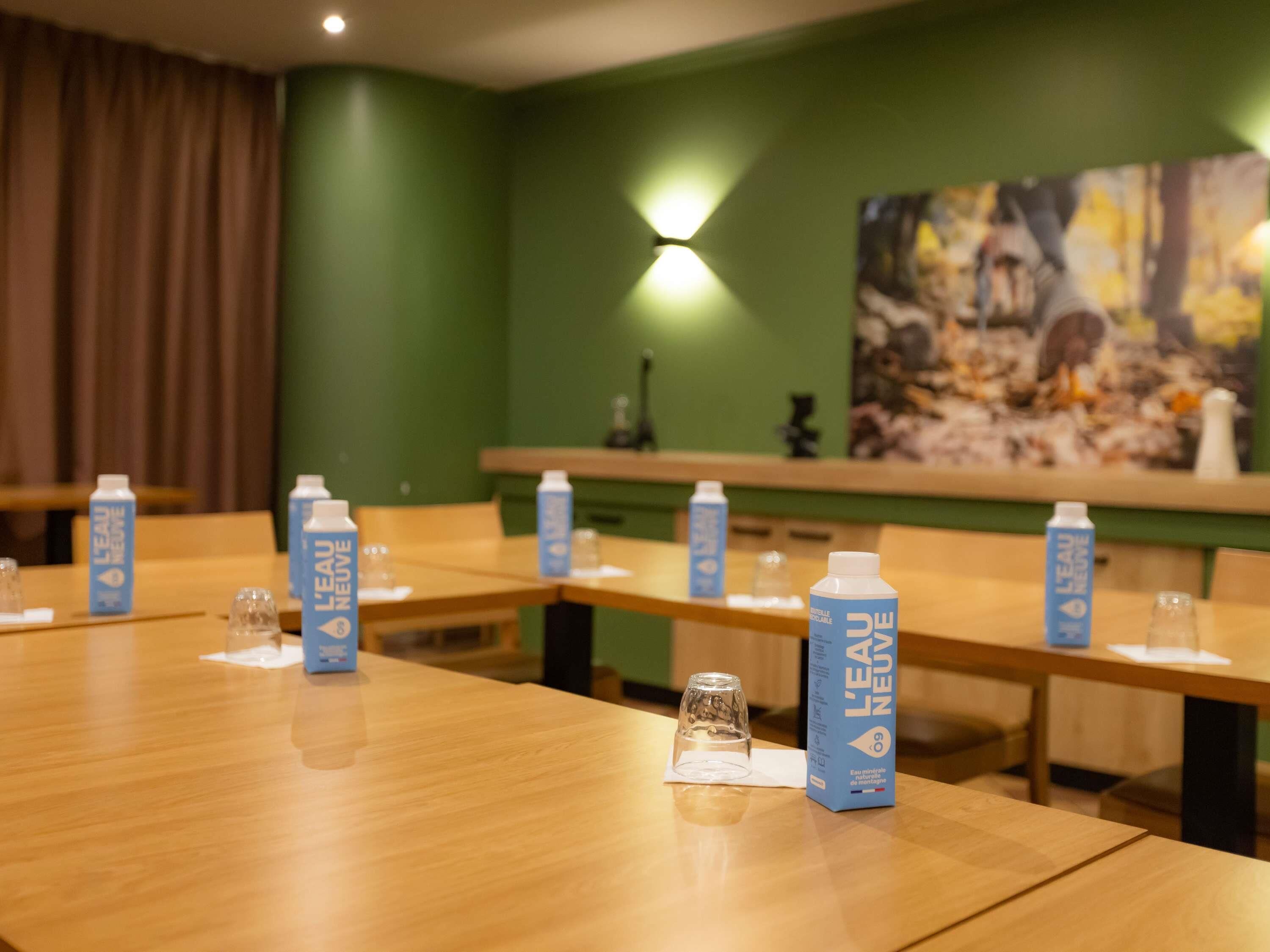 Un salón de conferencias con mesas, botellas de agua y un cuadro en la pared.