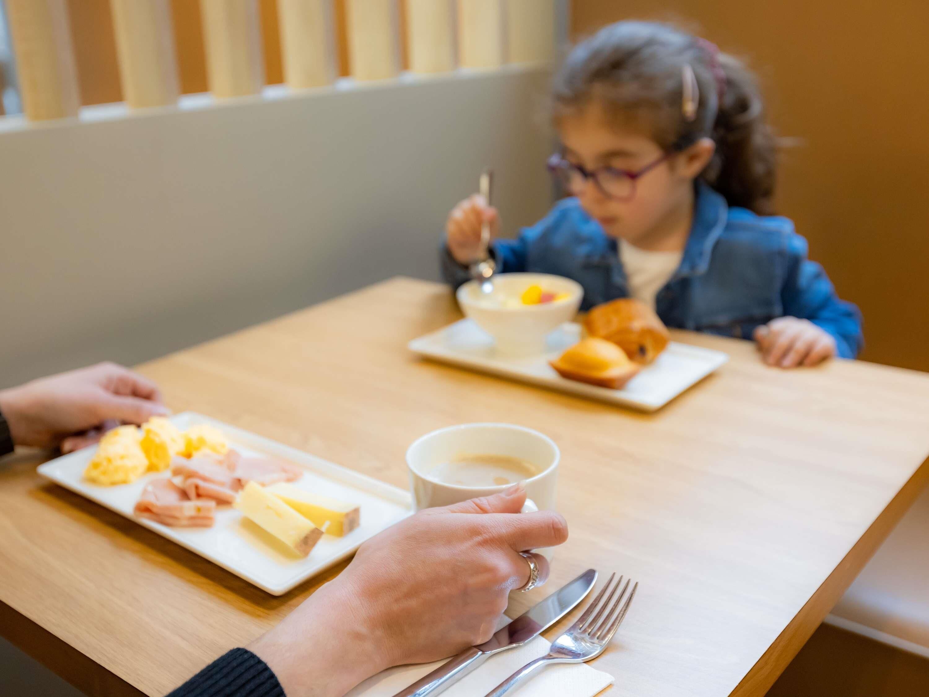 Une personne tenant une tasse de café, une assiette de nourriture et une fourchette sur une table en bois.
