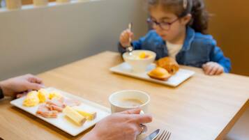 Une personne tenant une tasse de café, une assiette de nourriture et une fourchette sur une table en bois.