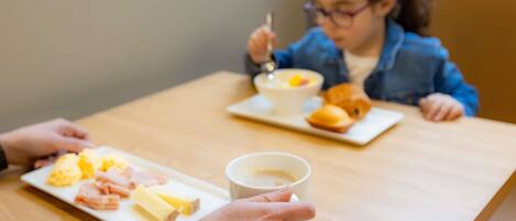Una persona sosteniendo una taza de café, un plato de comida y un tenedor sobre una mesa de madera.
