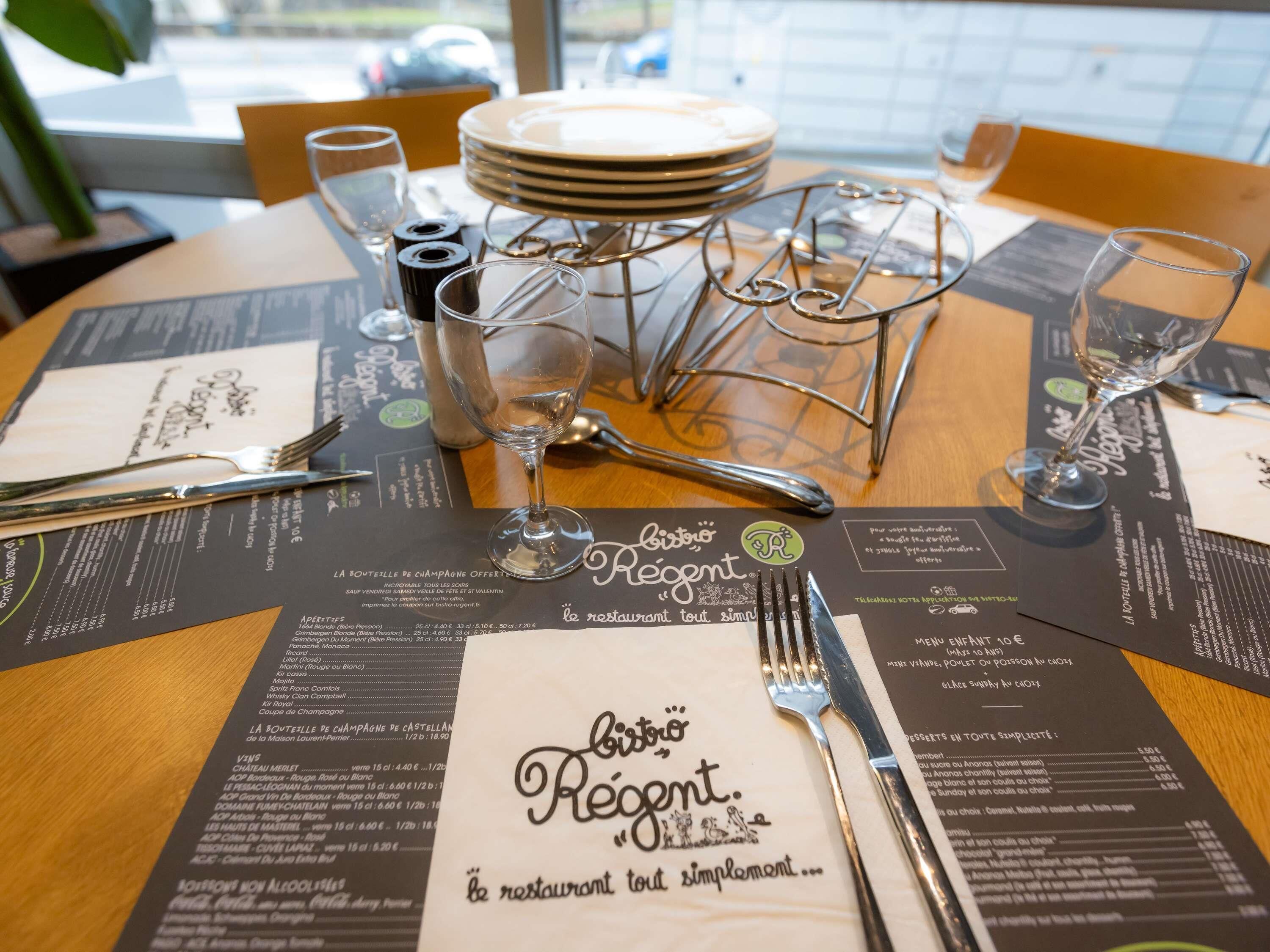 Ambiente de restaurante com menu, copos de vinho e talheres sobre a mesa.