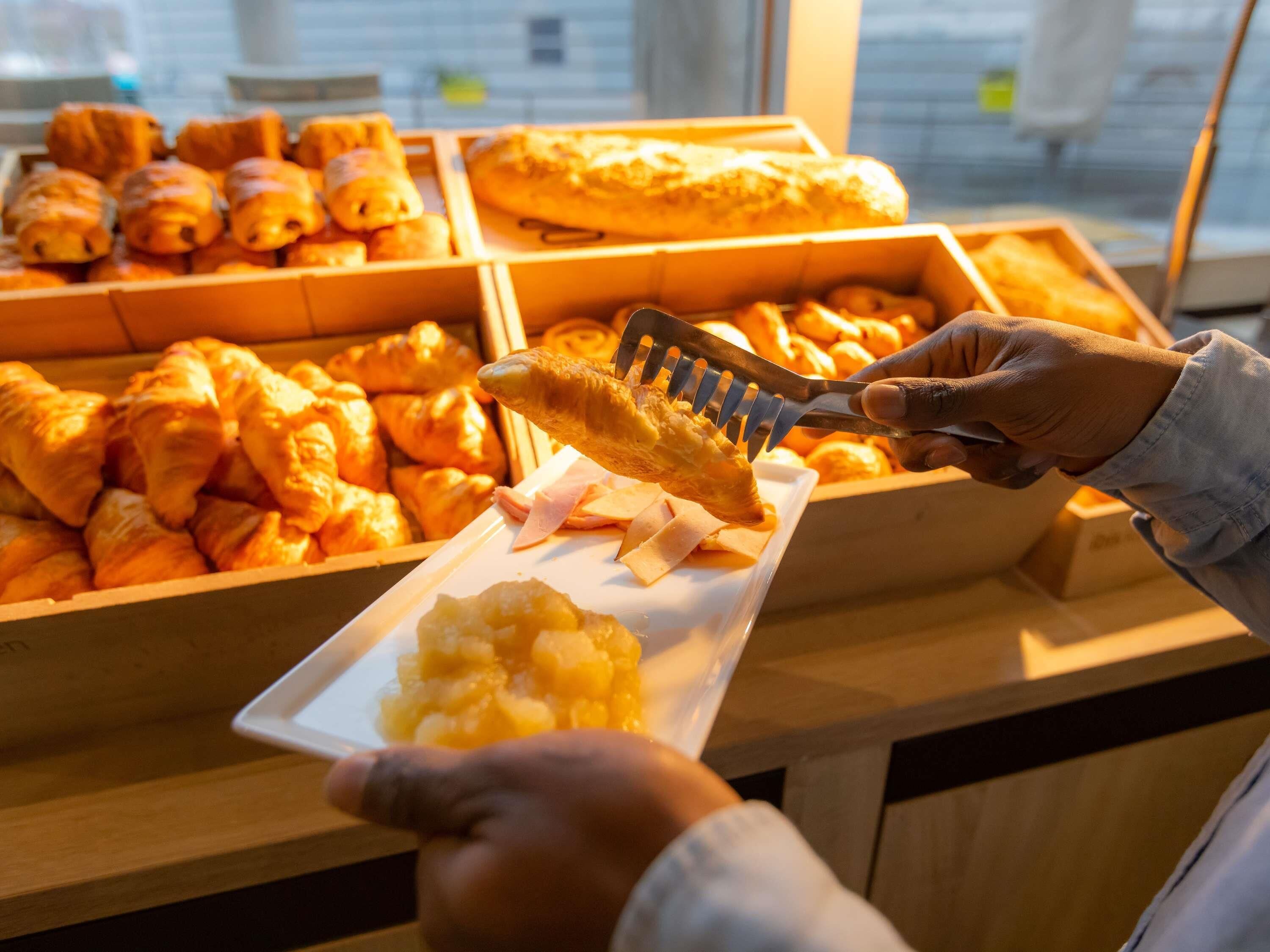A person serving a croissant from a wooden box filled with various pastries.