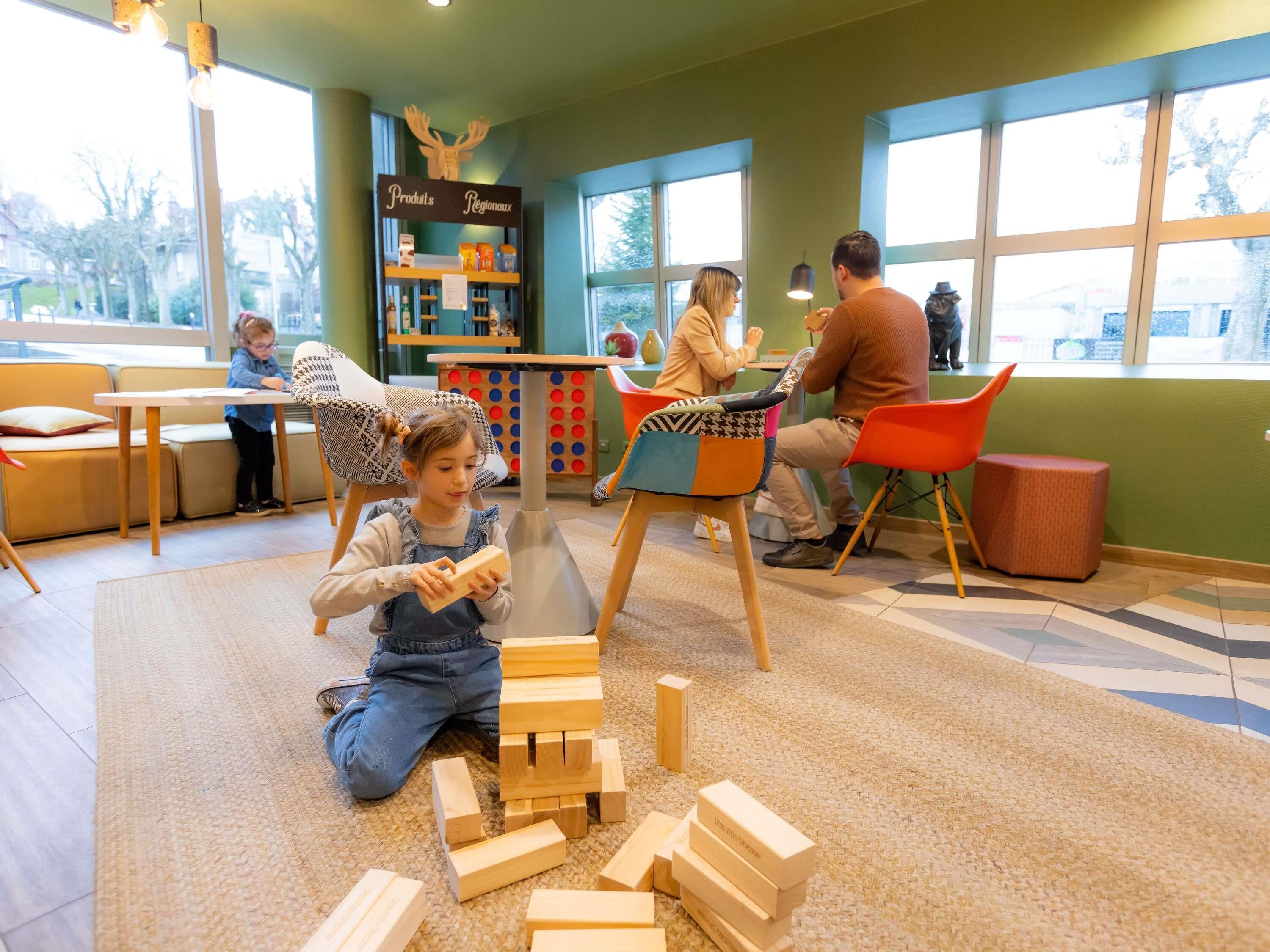 Een kinderspeelruimte met houten blokken, een boekenplank en een tafel met stoelen.