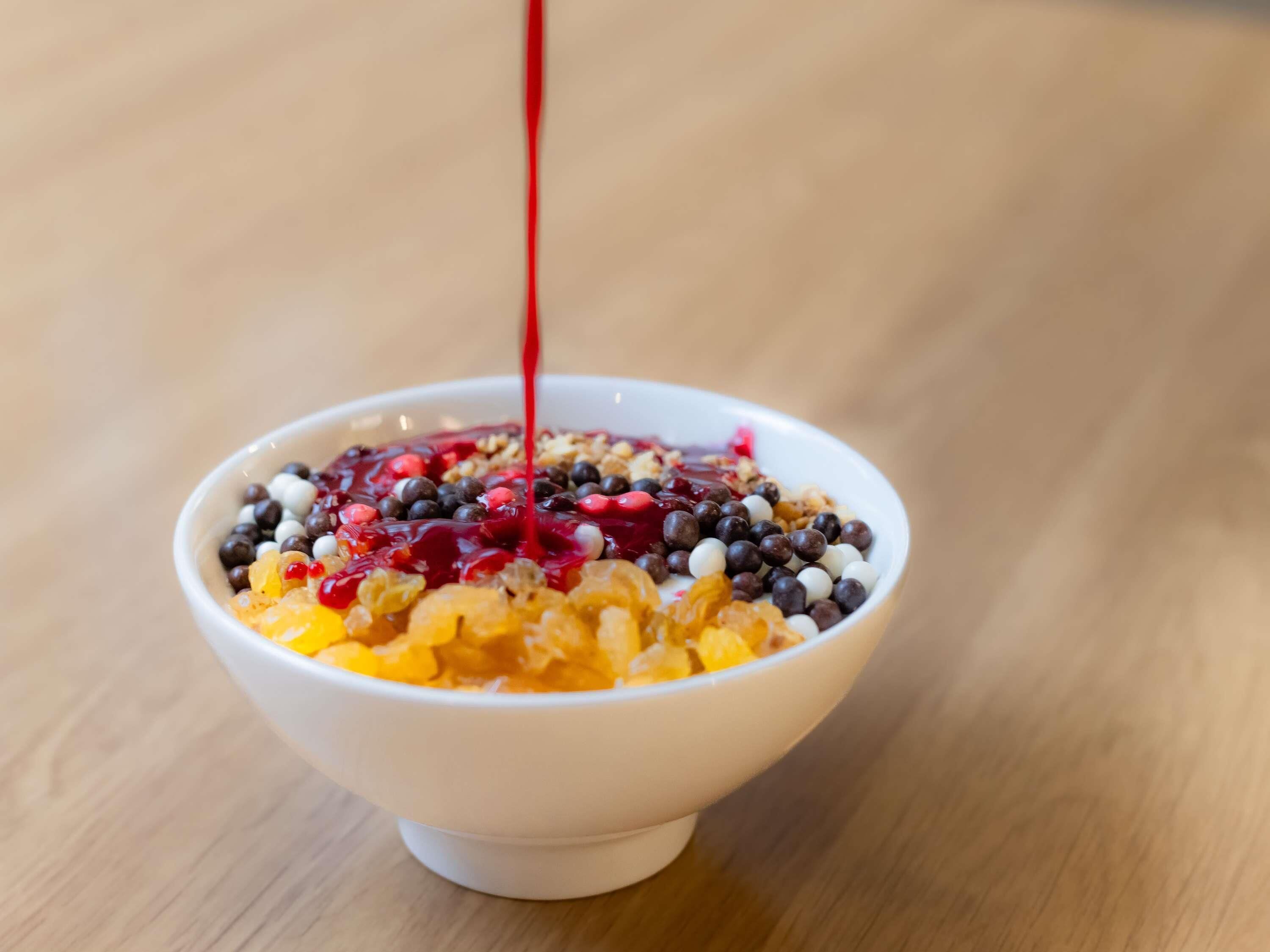 A bowl of cereal with various toppings and a red liquid being poured into it.