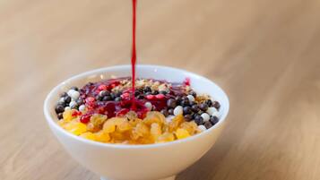 A bowl of cereal with various toppings and a red liquid being poured into it.