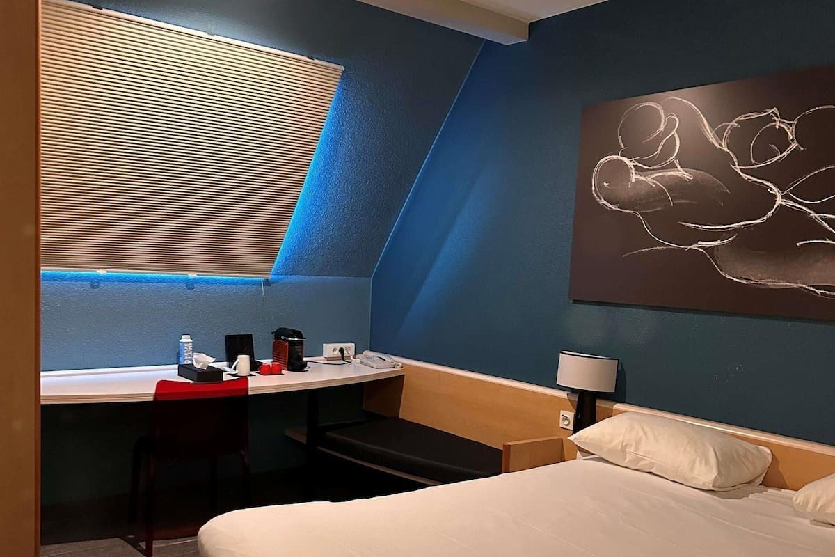 Ein Hotelzimmer mit Bett, Schreibtisch, Stuhl, Lampe und einem Bild an der Wand.