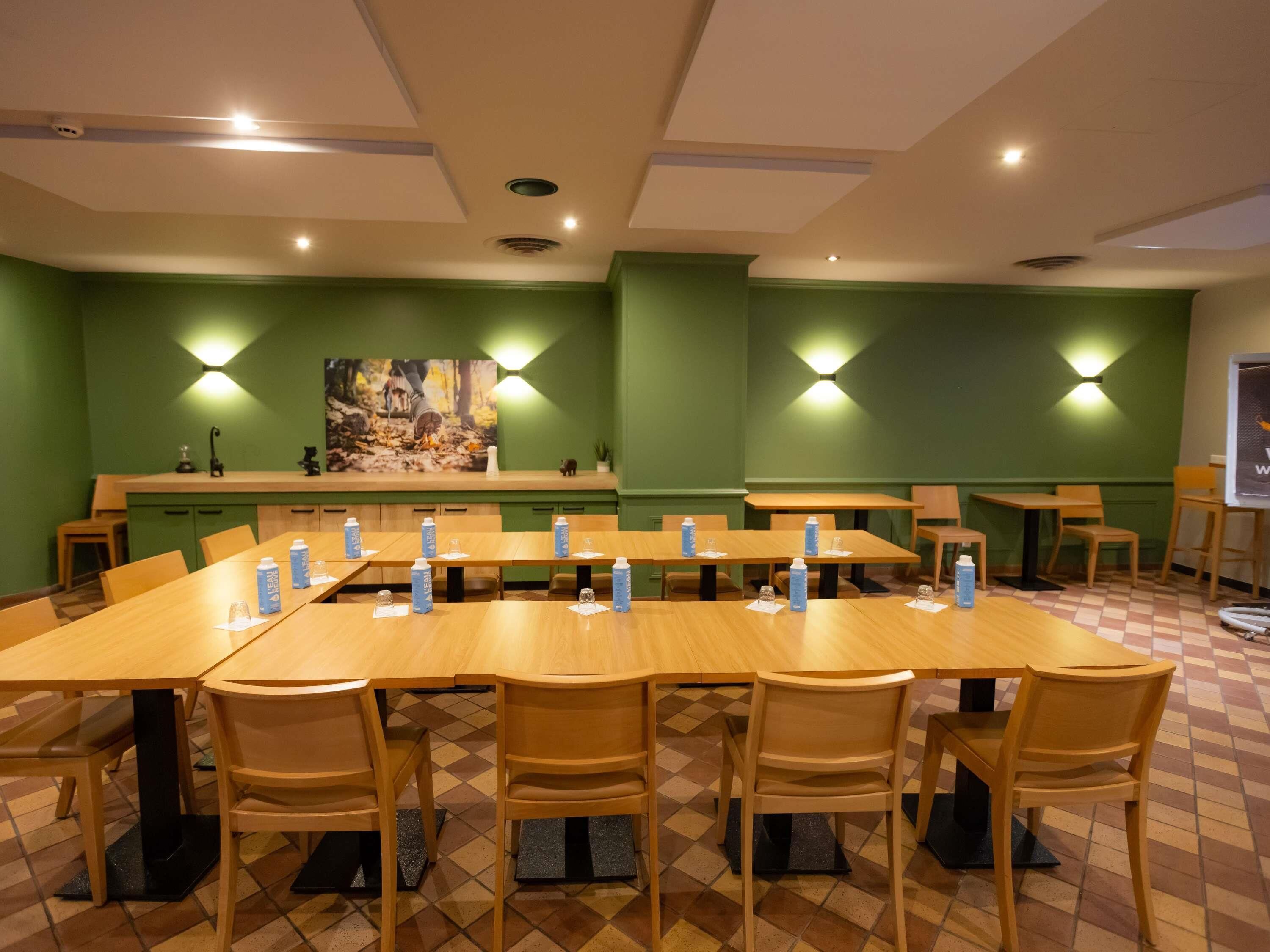 Un salón de conferencias con varias mesas y sillas, paredes verdes e iluminación empotrada.
