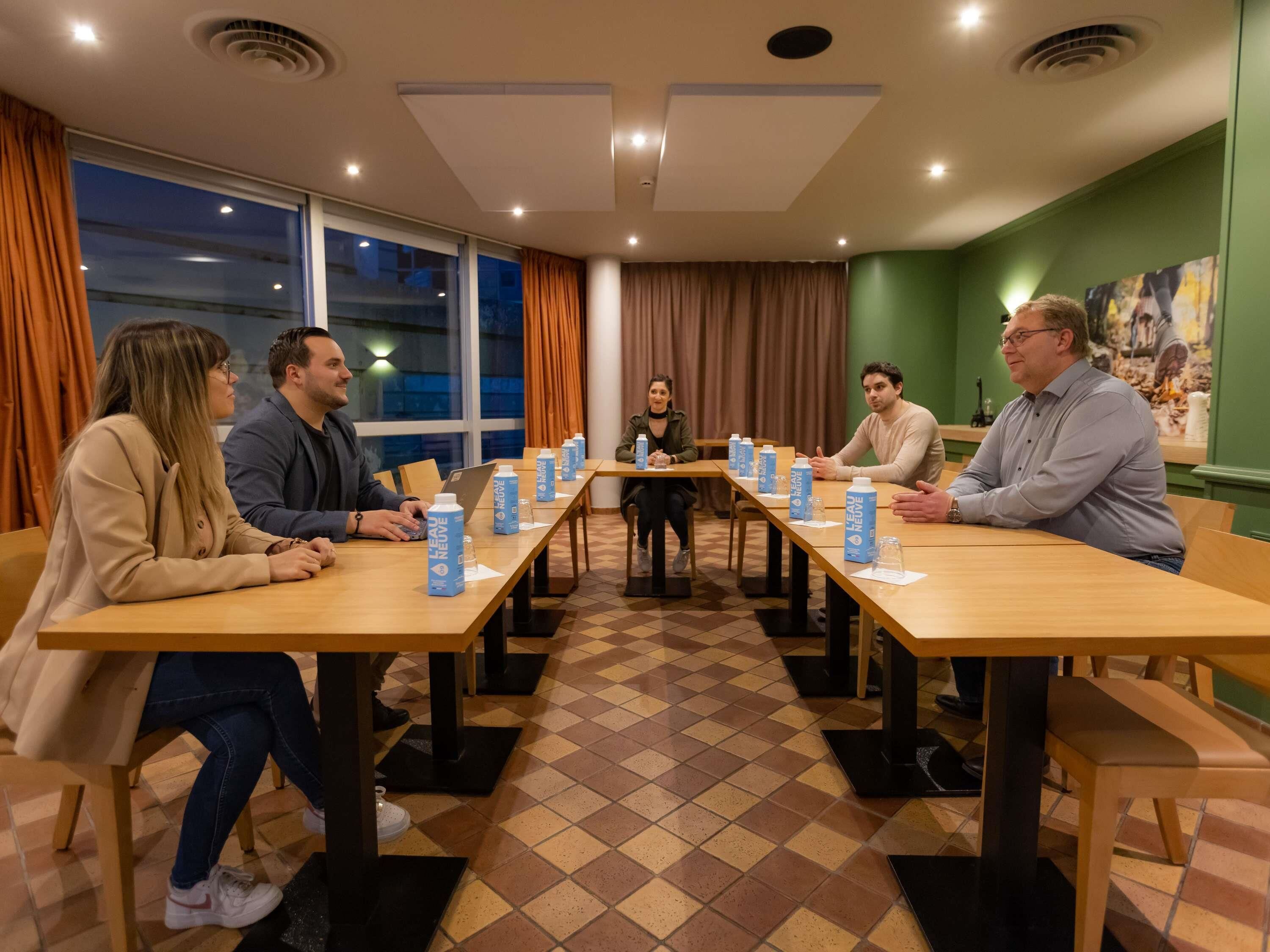 A conference room with a long table, chairs, and a person standing in the center.
