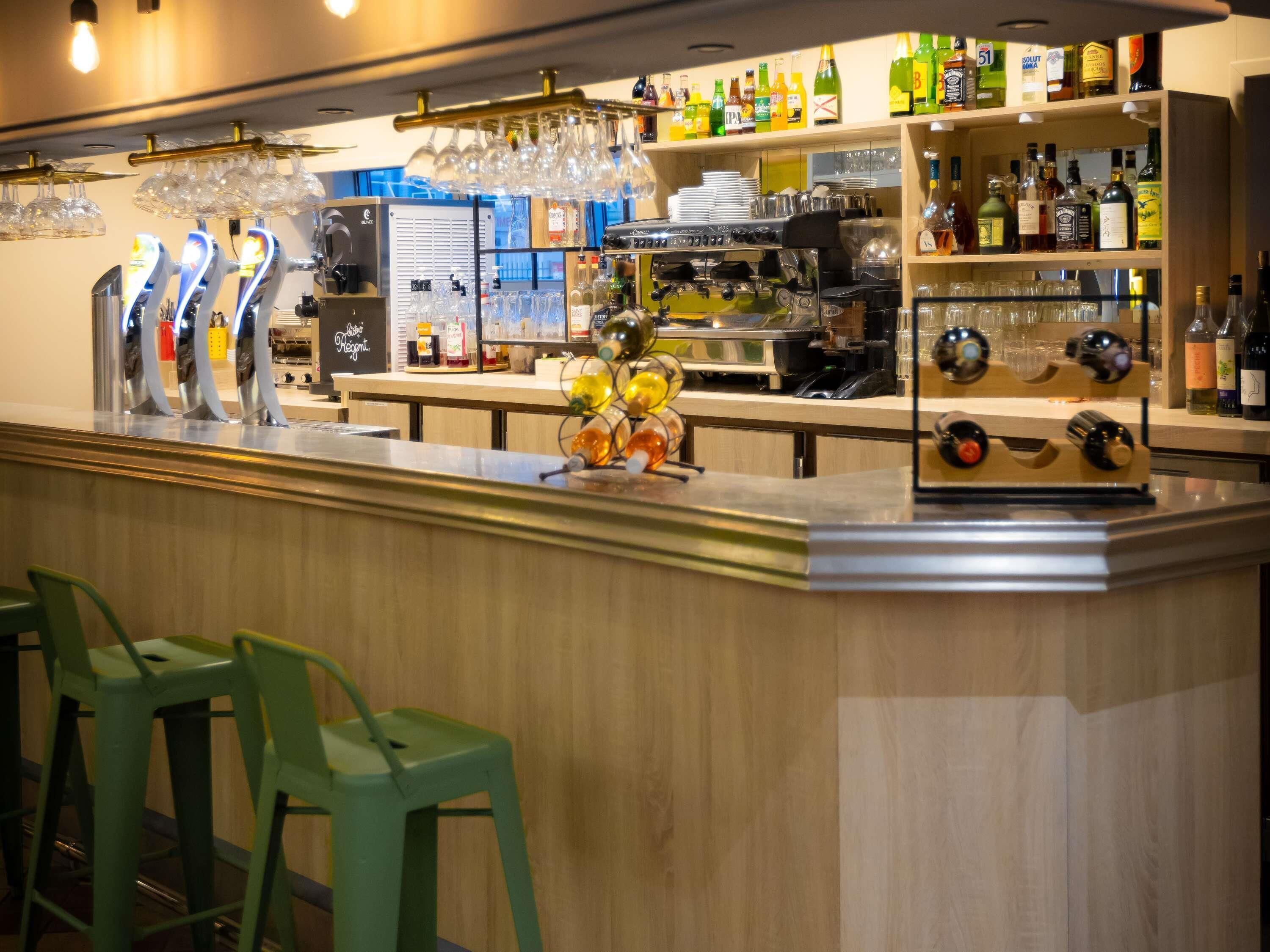 Een bar met een toog, barstoelen, een koffieapparaat en planken met flessen en glazen.