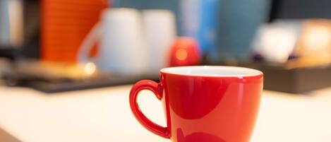 A red mug on a white surface with a blurred background of various objects.