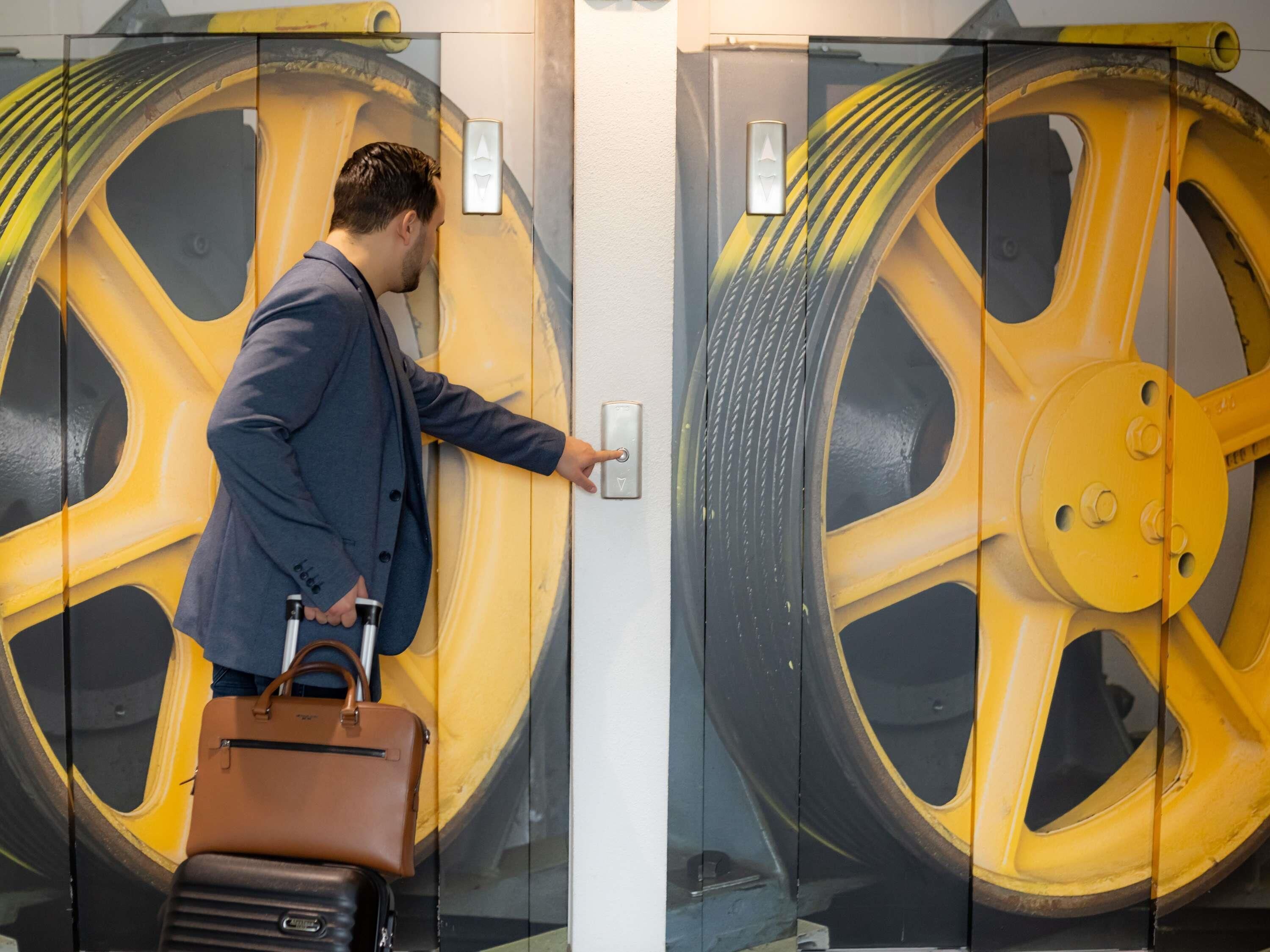 Un hombre con traje y maletín, de pie frente a una puerta con un llamativo diseño de rueda amarilla.