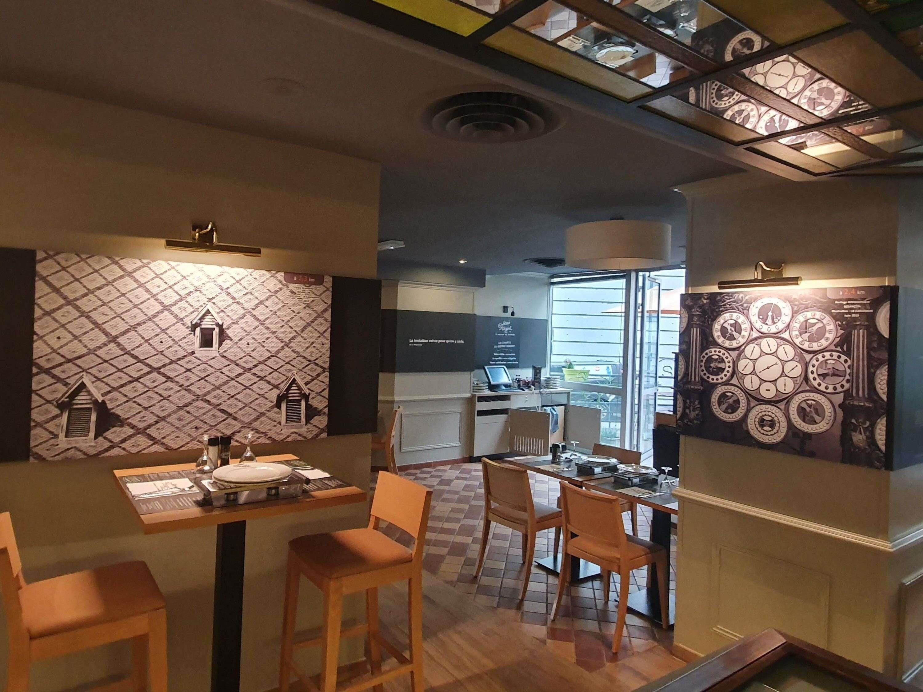 Un restaurant avec un sol à carreaux, des chaises en bois, une table avec une assiette et des couverts, et un mur décoré d’un motif représentant des horloges.
