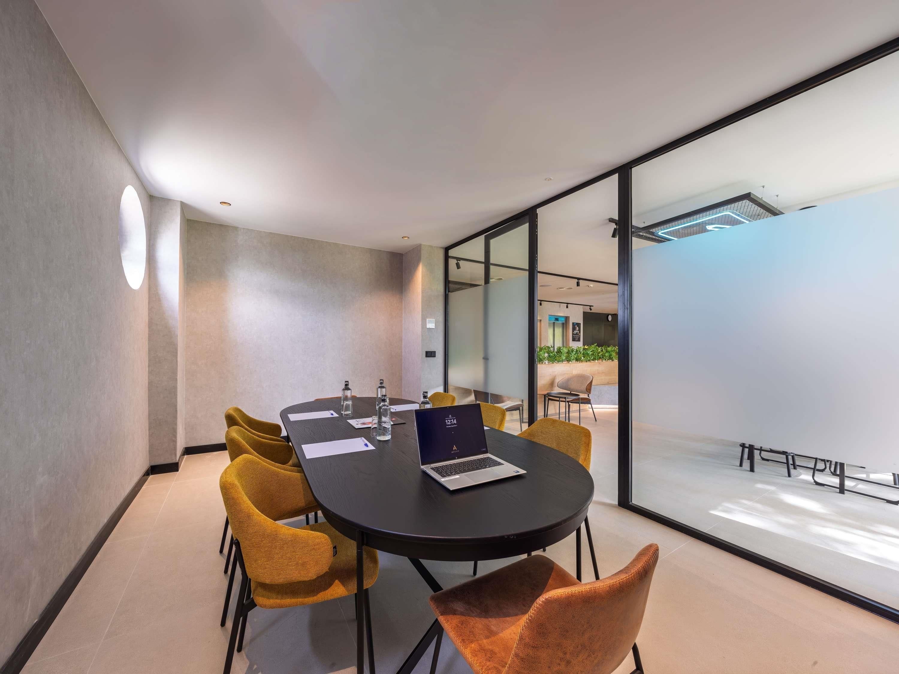 A modern conference room with a round table, yellow chairs, and a laptop.