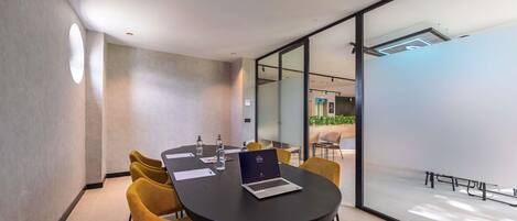 A modern conference room with a round table, yellow chairs, and a laptop.