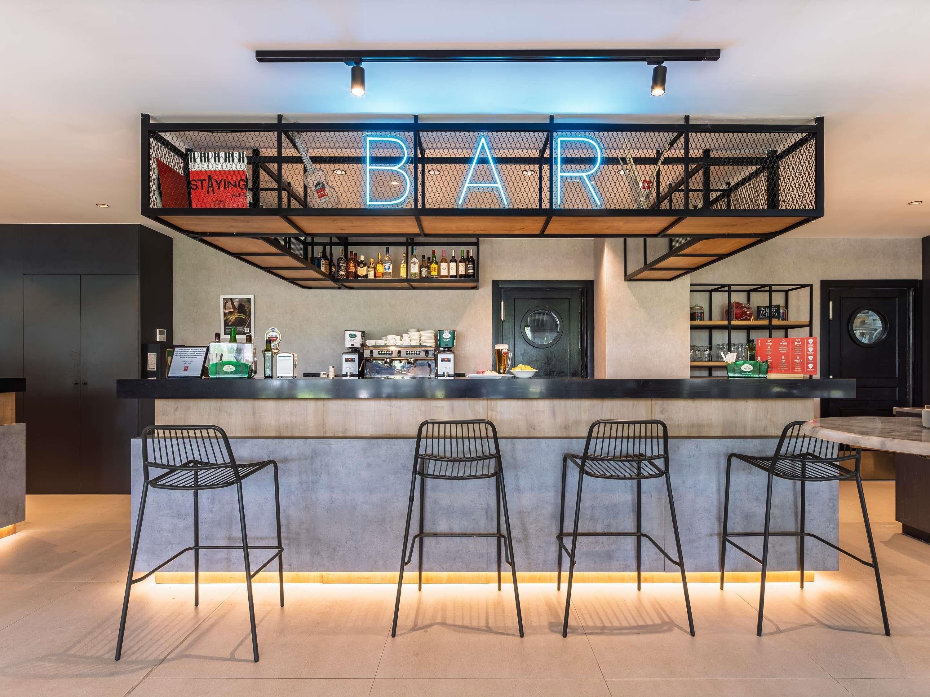 Zona de bar con mostrador, taburetes y una variedad de botellas.