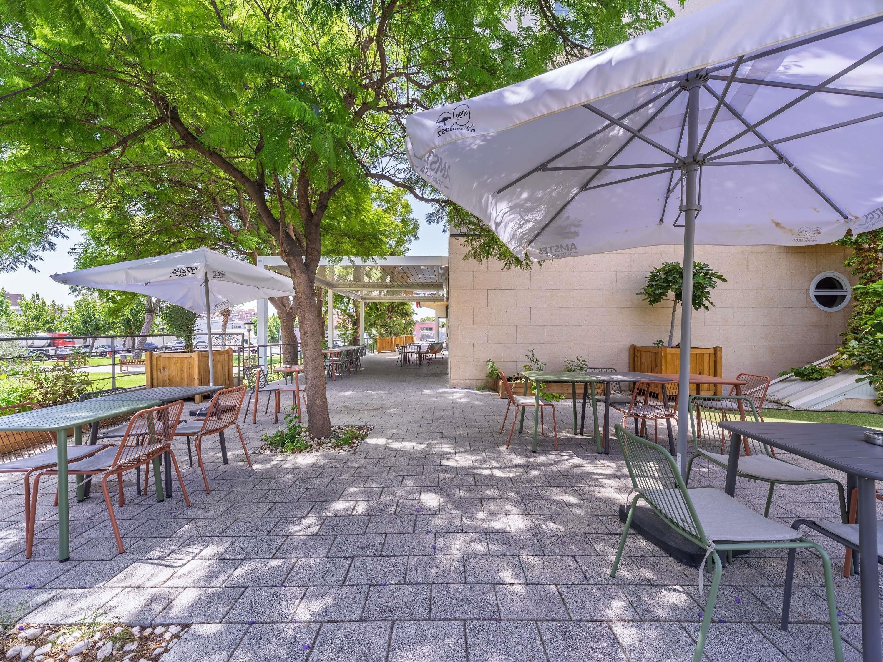 Un patio al aire libre con mesas, sillas, sombrillas y vista a un estacionamiento.