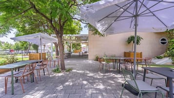 Eine Außenpatio-Terrasse mit Tischen, Stühlen, Sonnenschirmen und Blick auf einen Parkplatz.