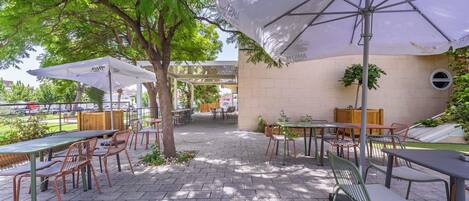 Un patio al aire libre con mesas, sillas, sombrillas y vista a un estacionamiento.