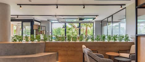 Un interior moderno con una mesa de recepción, zona de estar y ventanas amplias que ofrecen vista a zonas verdes.