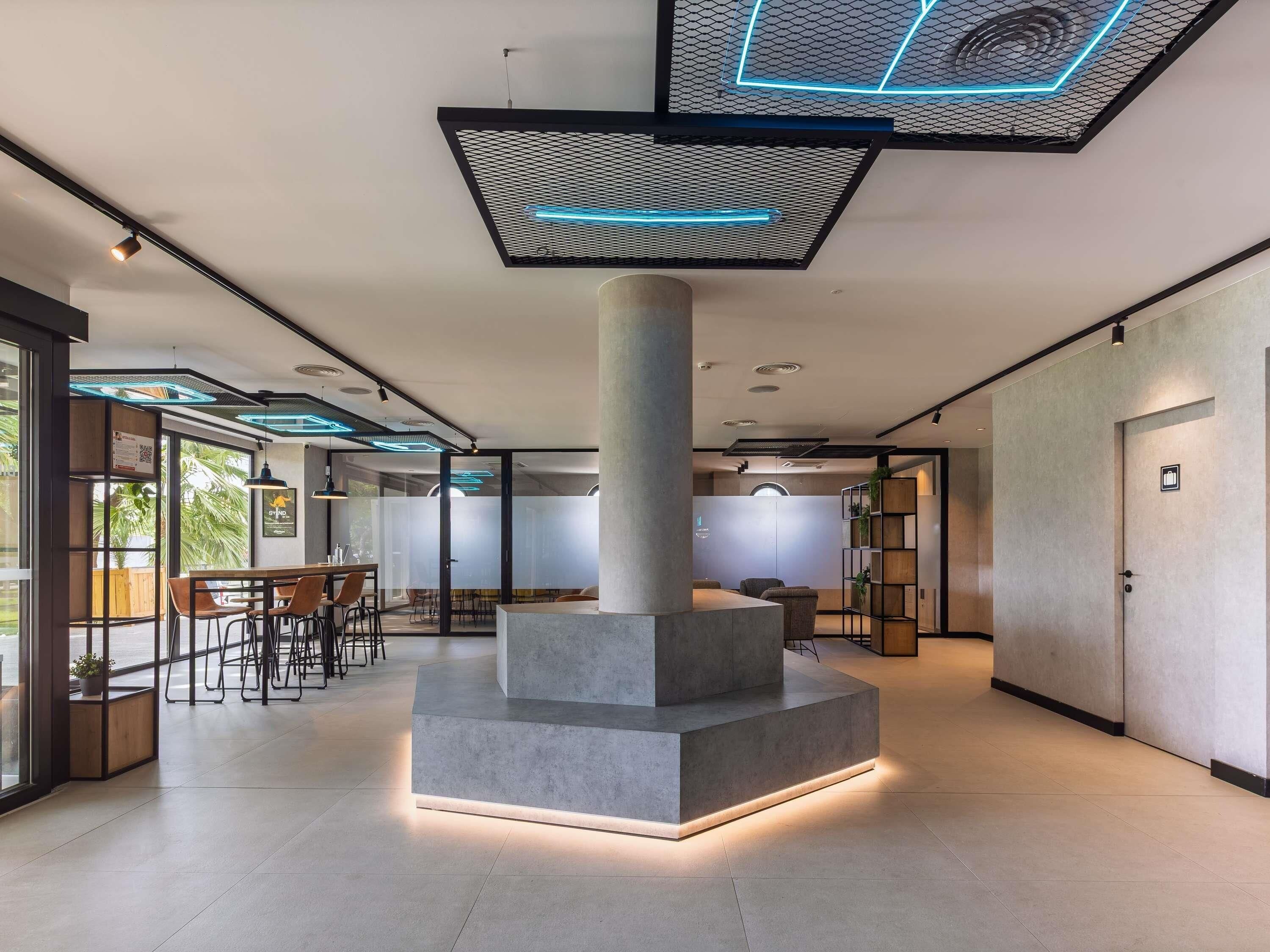 Ein modernes Interieur mit einer zentralen Säule, Glaswänden und einer Sitzecke mit Tischen und Stühlen.