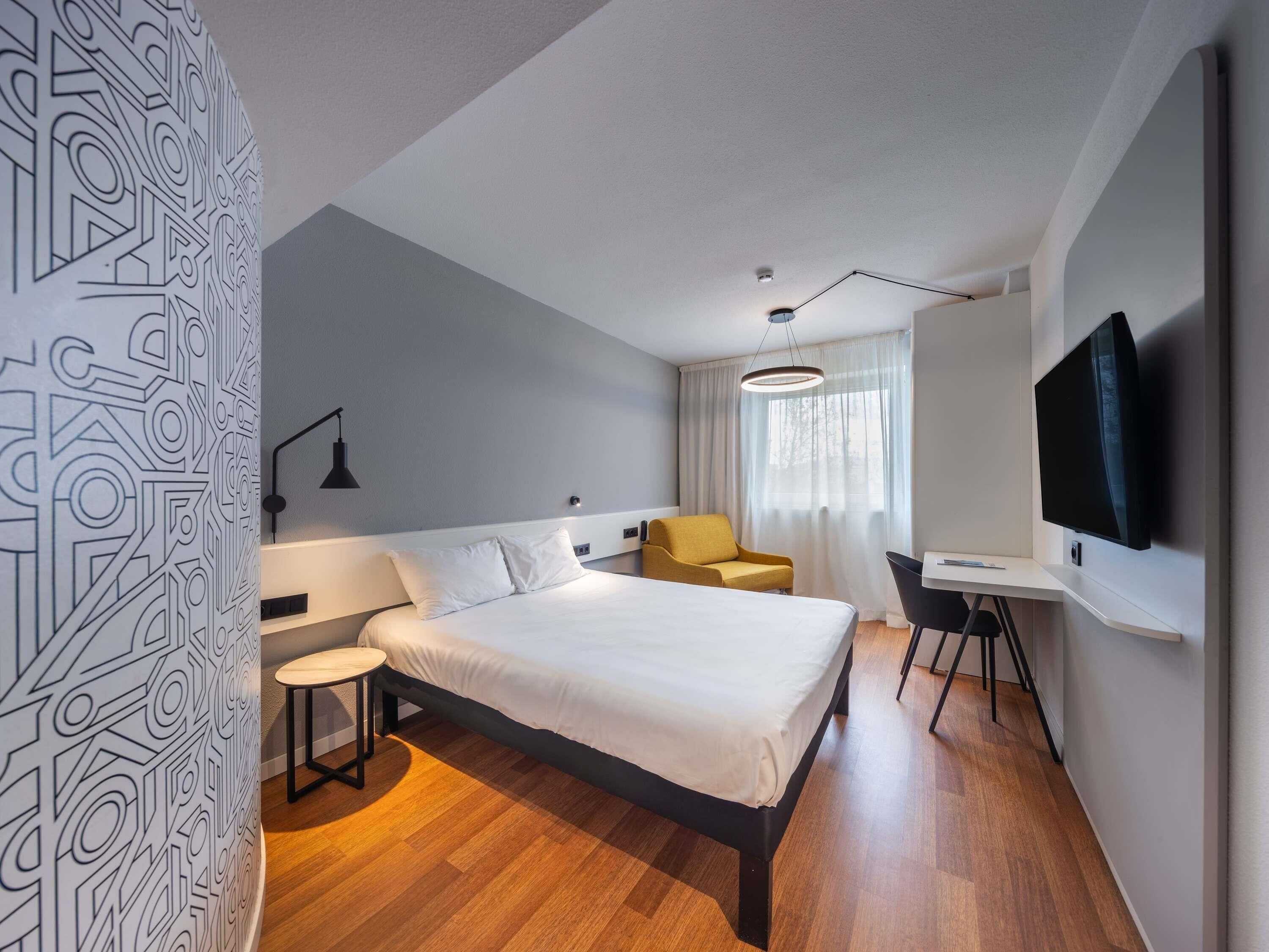 Una habitación de hotel moderna con cama, escritorio, silla, televisor y pared con diseño.