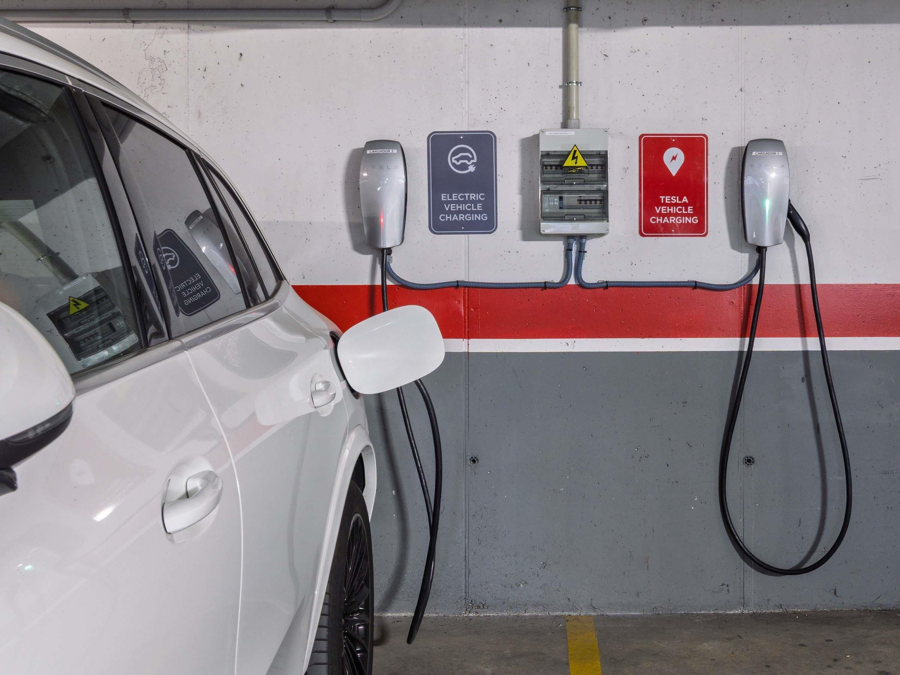 A parking garage with electric vehicle charging stations, a car parked, and a red and white striped wall.