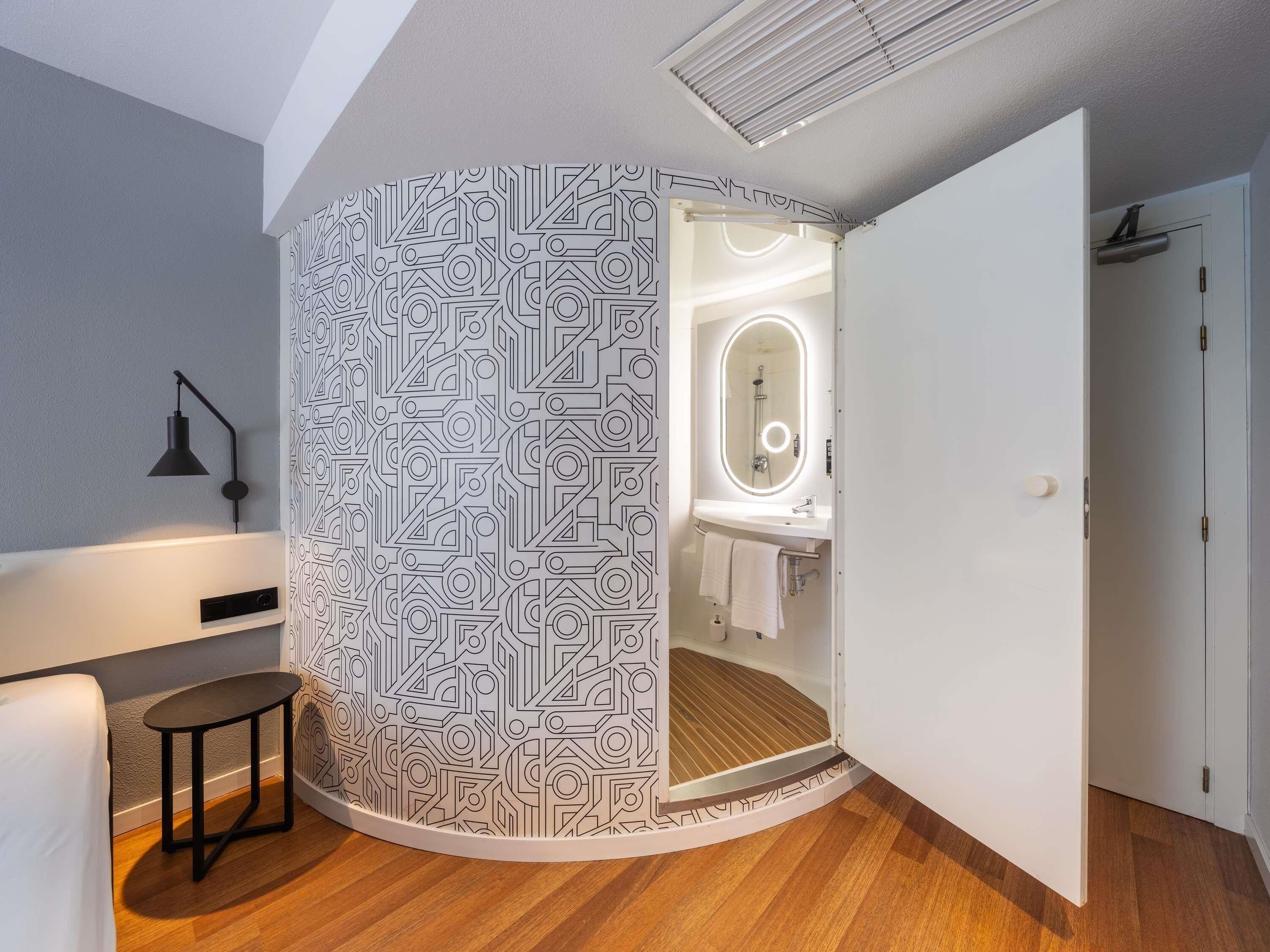 A modern bathroom with a geometric patterned wall, a vanity with a mirror, and a shower.