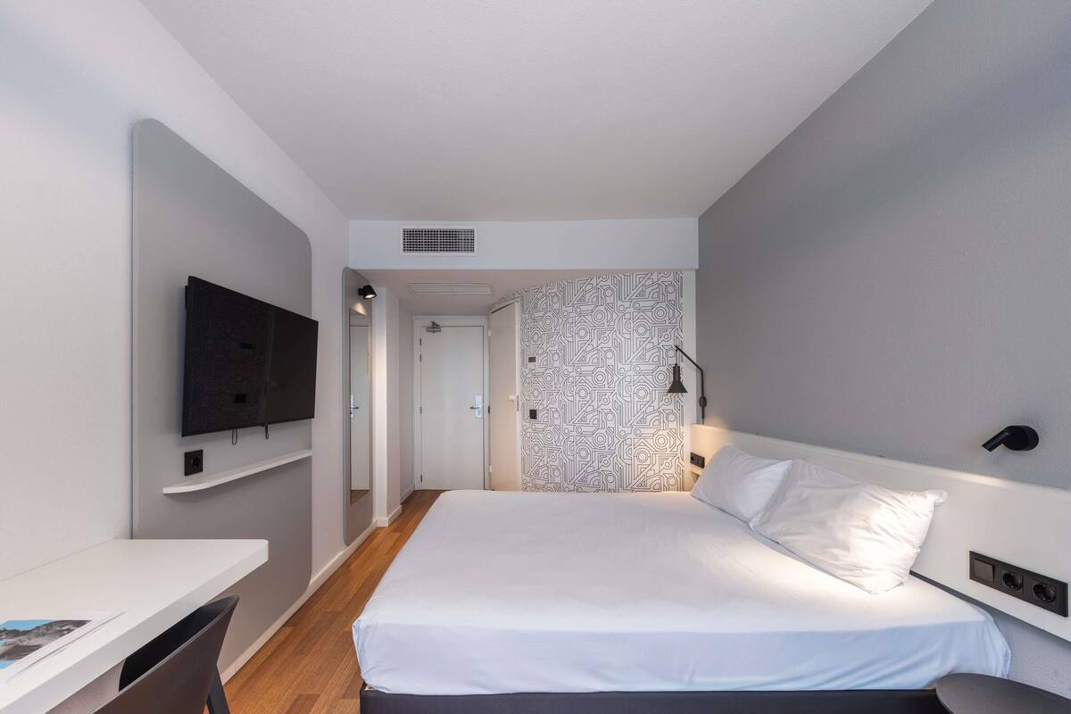 Ein modernes Hotelzimmer mit einem Bett, einem Schreibtisch, einem Fernseher und einer Wand mit Muster.