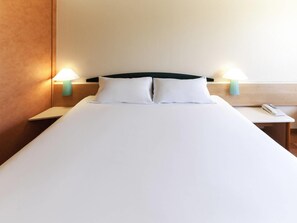 A hotel room with a bed, two bedside lamps, a nightstand, and a phone.