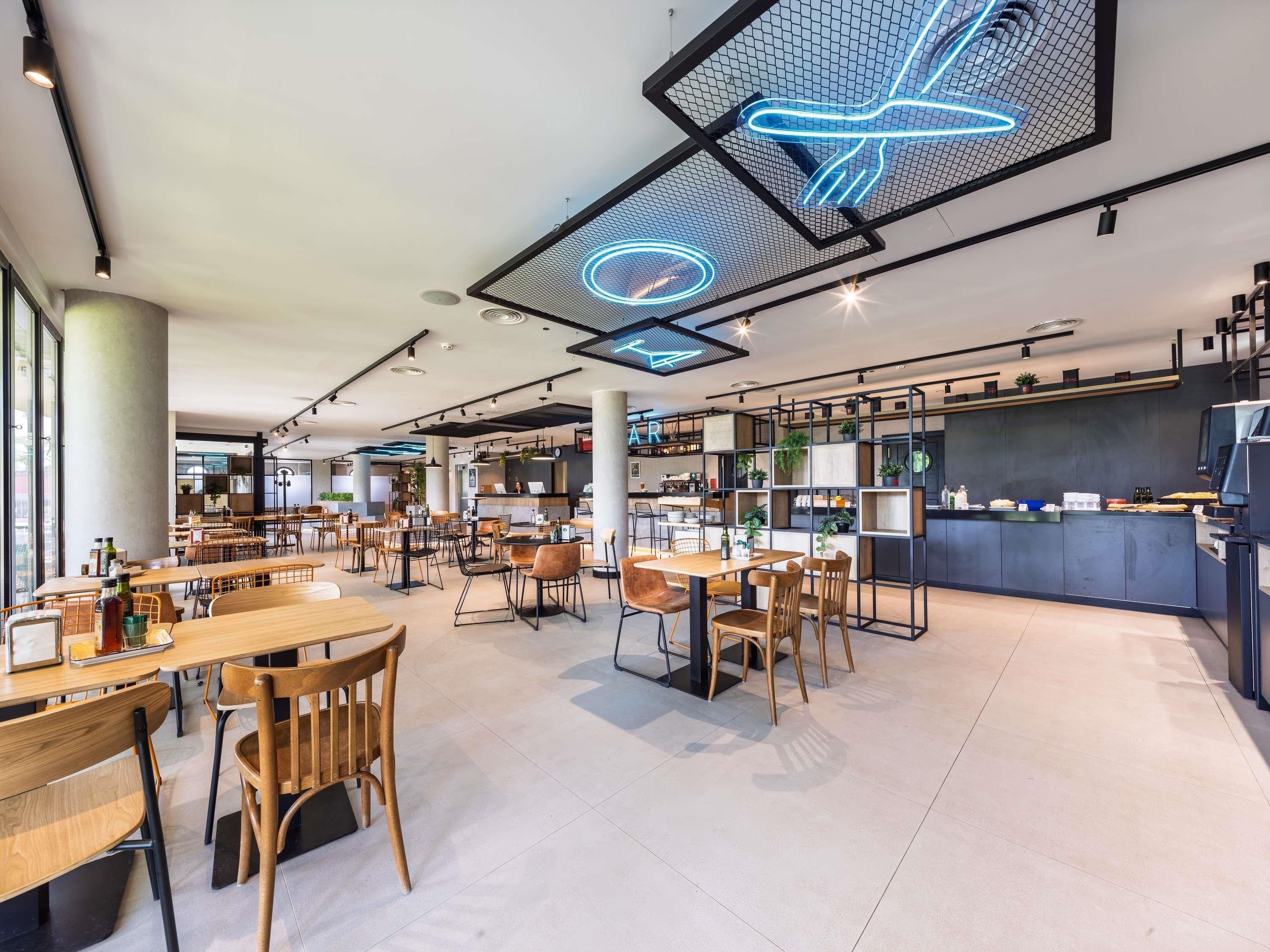 Un caffè moderno con tavoli e sedie in legno, un bancone con il menù e un neon a illuminare il soffitto.