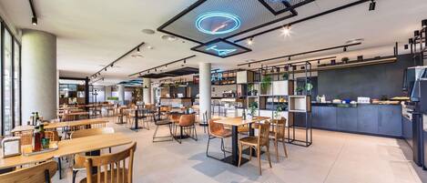 A modern cafe with wooden tables and chairs, a counter with a menu, and a neon sign on the ceiling.