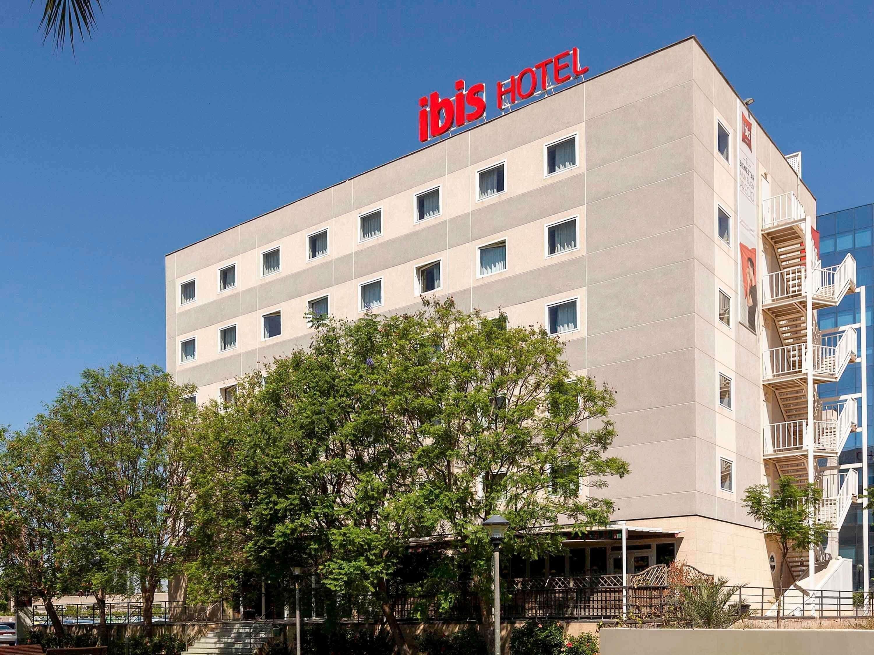 Un bâtiment d’hôtel à la façade plate, doté de nombreuses fenêtres et d’une enseigne indiquant « ibis HOTEL » en haut.