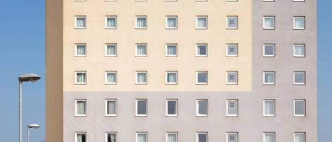 A multi-story hotel with a uniform facade, featuring a series of windows and a prominent 'ibis HOTEL' sign at the top.