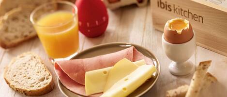 Ein Frühstück mit Brot, Eiern, Käse, Schinken und Saft auf einem Holztisch.