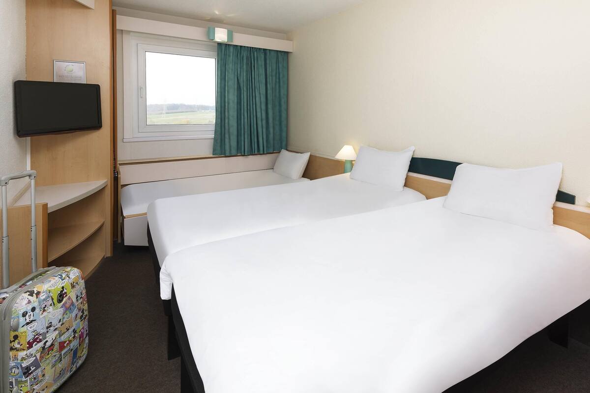 Une chambre d’hôtel avec deux lits, une télévision, une fenêtre avec des rideaux, un bureau et une chaise.